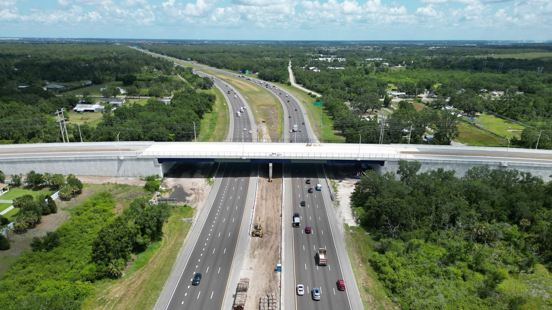 A bridge spans across a busy overpass, with vehicles traveling beneath its structure and clear sky in the background.