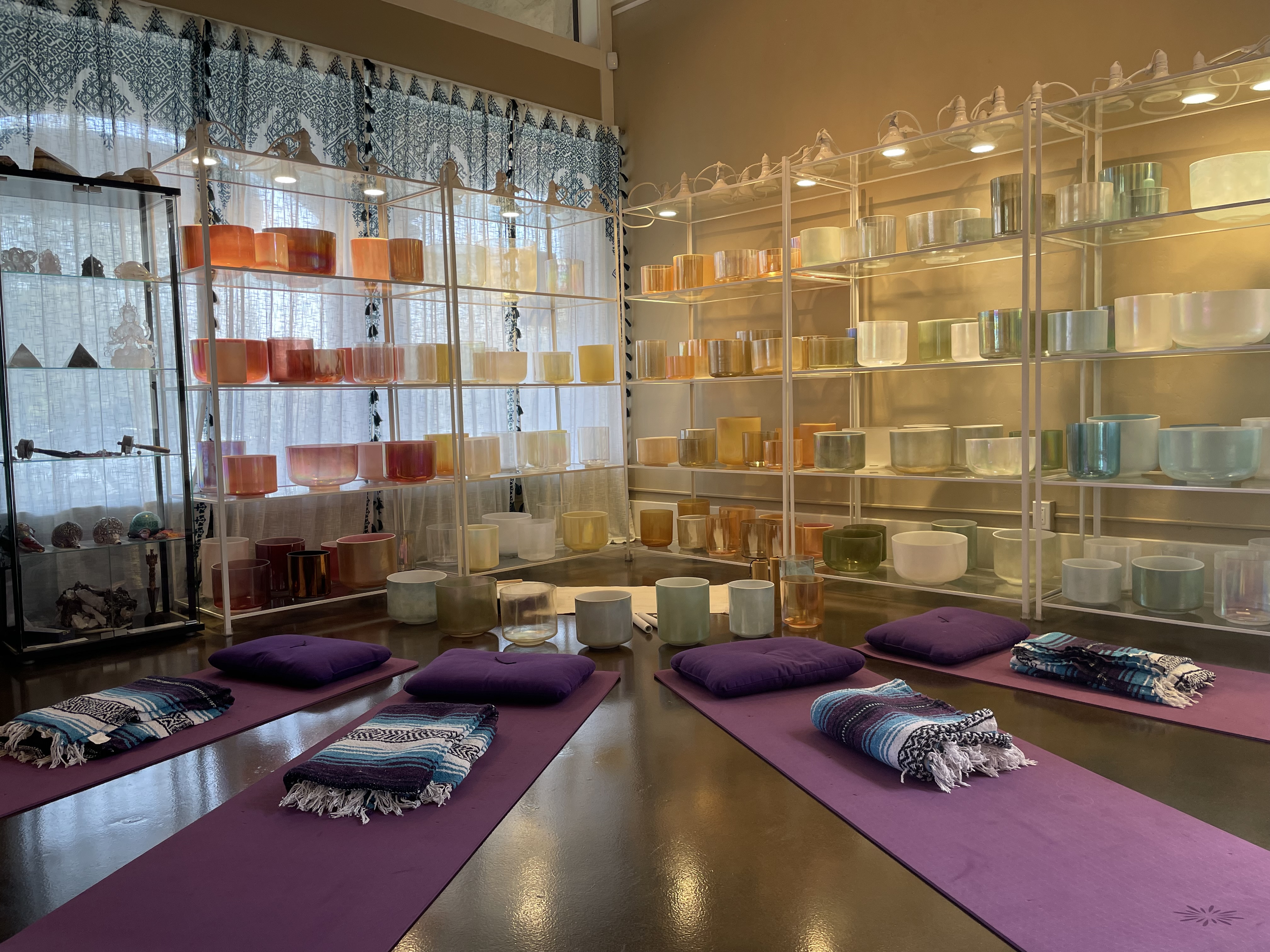 A set up of mats and props before sound bath participants joint at Sacred Sound of the Soul.  Special Crystal Tones Alchemy Crystal Singing Bowls are on the shelves in the background.