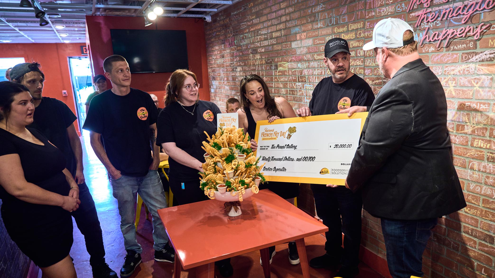 Joined by restaurant staff and his wife Cecilia Lanyon, Chef Dominic Zumpano accepts the Service Superstar Award from Chef Beau MacMillan, which included a customized fry bouquet from McCain Foods and a $20,000 reward intended to help The Peanut Gallery continue its support of the community and local first responders.