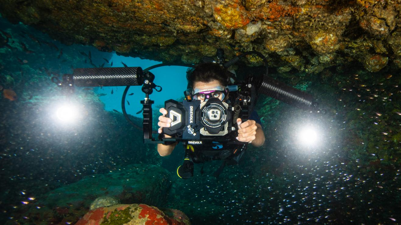 A diver frames a coral reef with a DIVEVOLK SeaTouch underwater smartphone housing, keeping a respectful distance from the reef