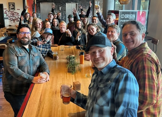 Image shows a group of 26 people at a restaurant toasting to the end of their leadership program