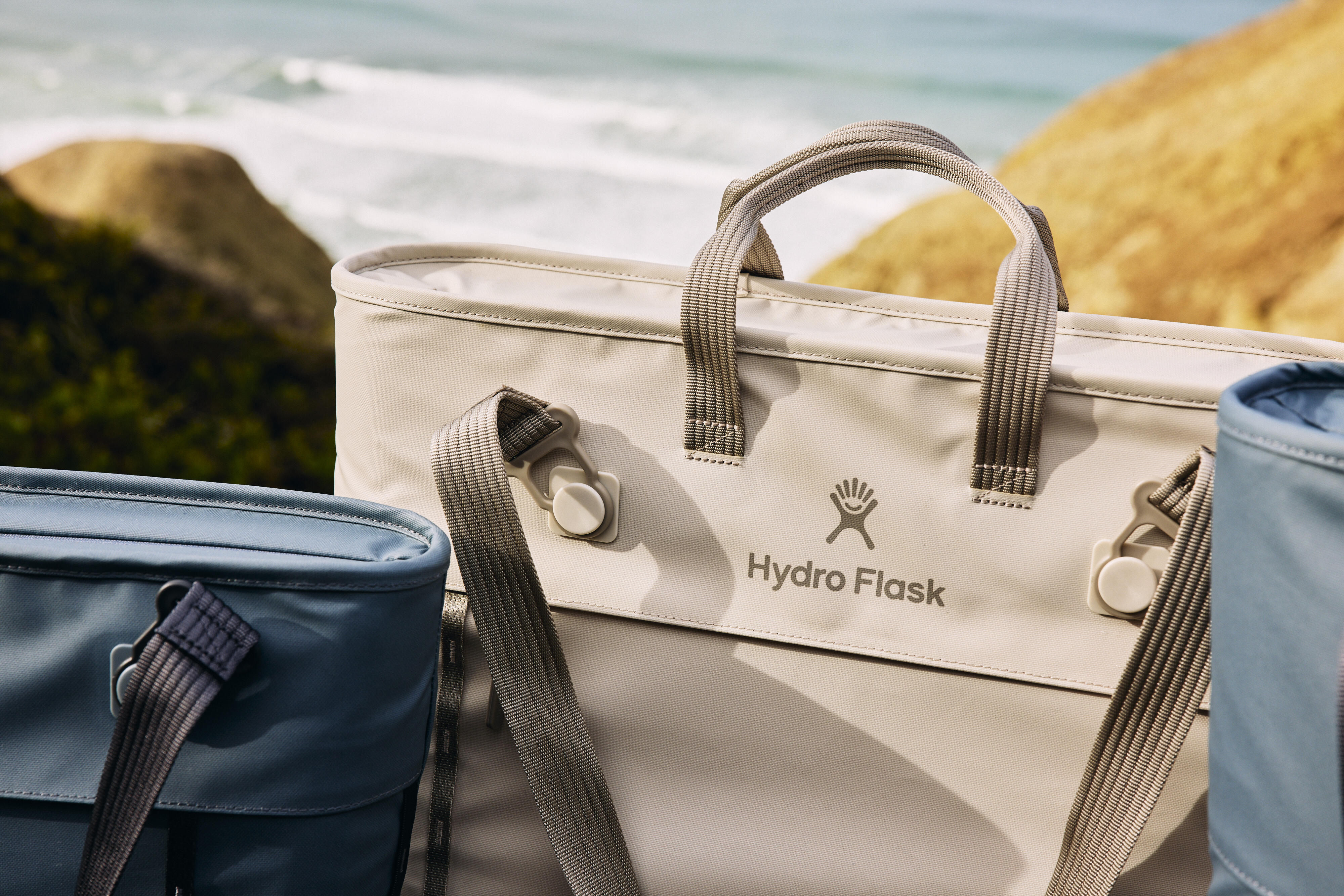 A close angle of a tan Hydro Flask Carryout™ Cooler Tote shows a removable strap detail.