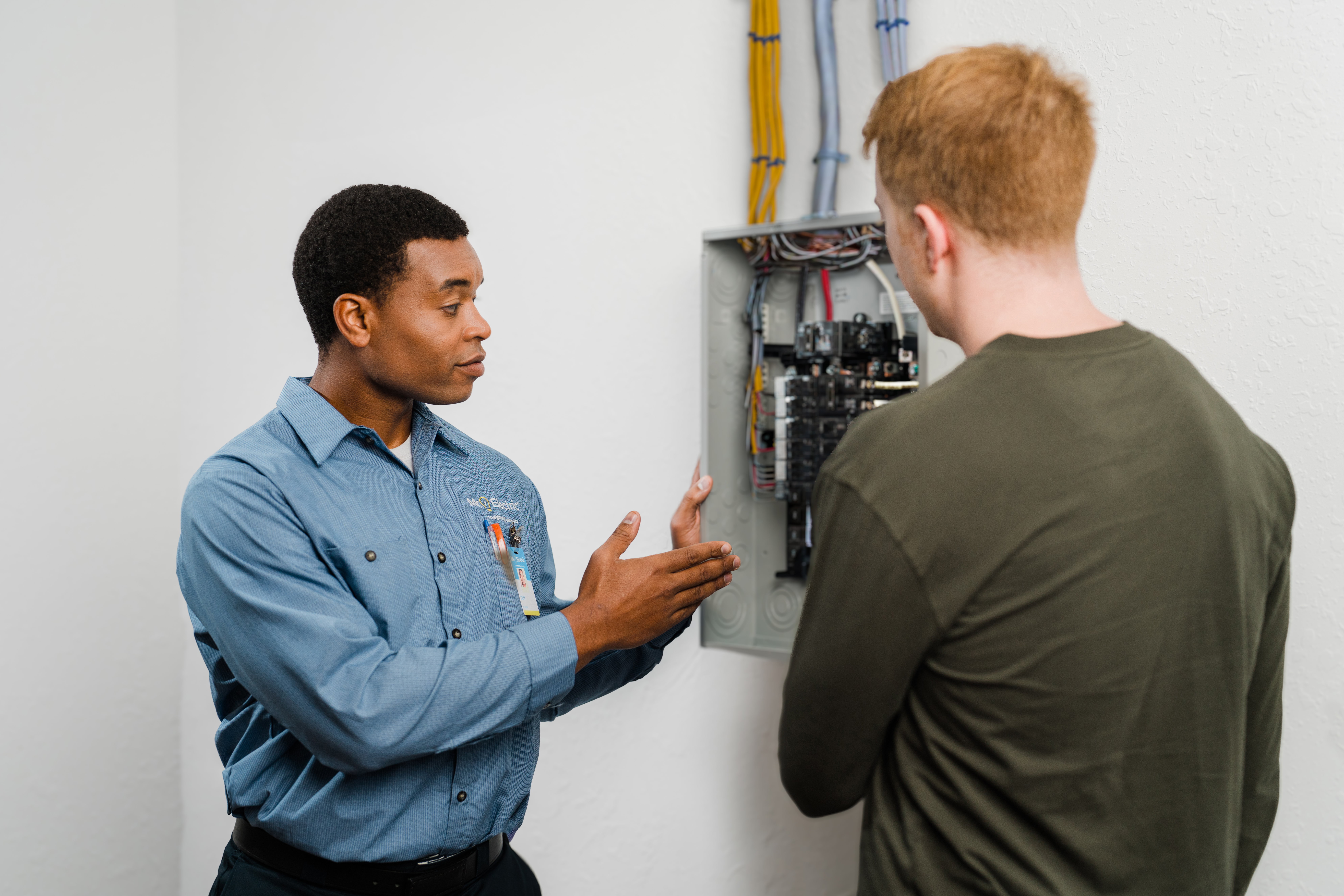 A Mr. Electric service professional is showing a homeowner their electrical panel and sharing safety tips.