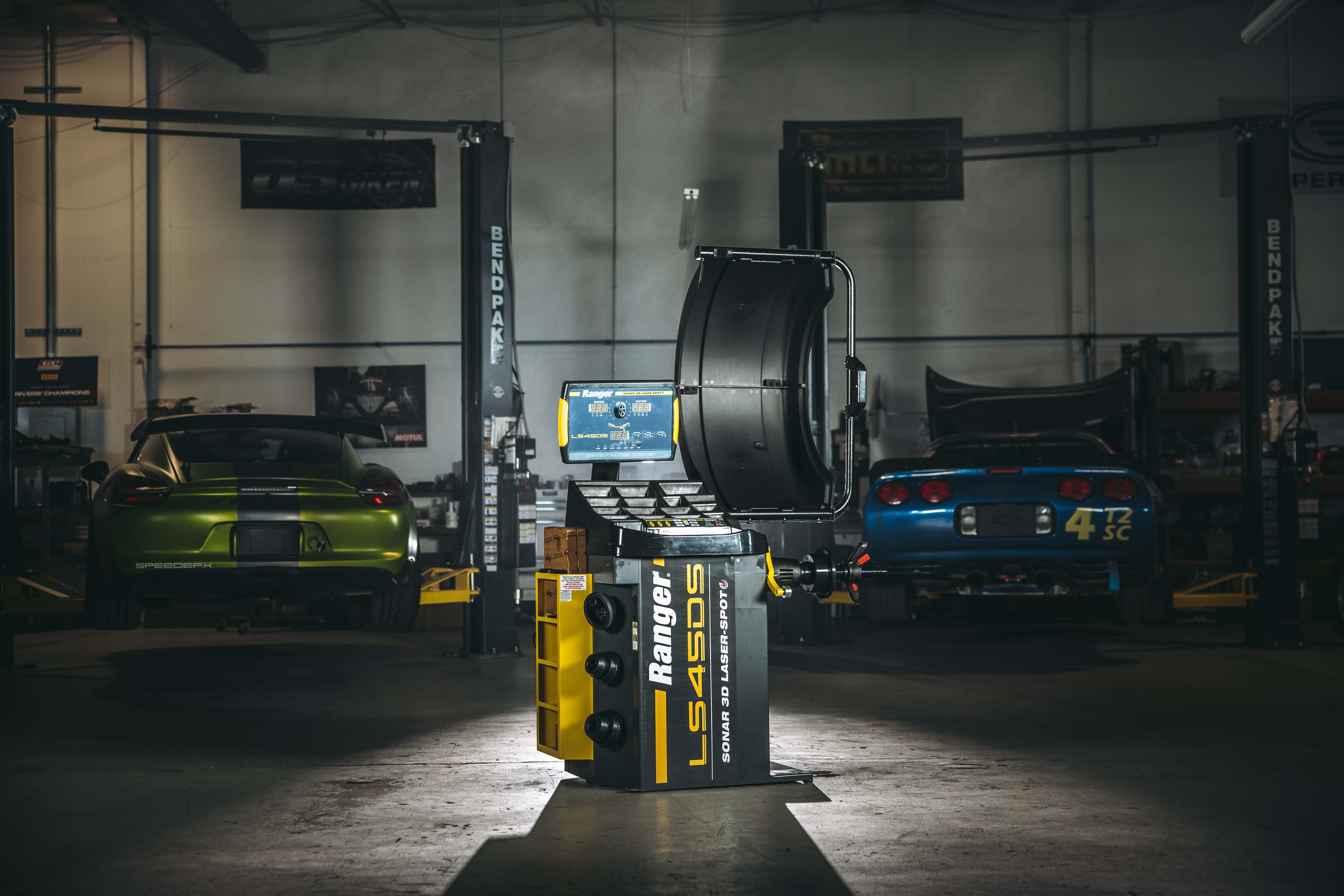 Ranger LS45DS wheel balancer stands spotlighted in front of BendPak two-post lifts in a darkened repair shop 