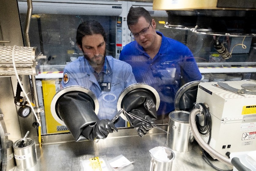 Lightbridge and INL team performing a visual inspection of a finished enriched uranium-zirconium coupon sample inside a glovebox