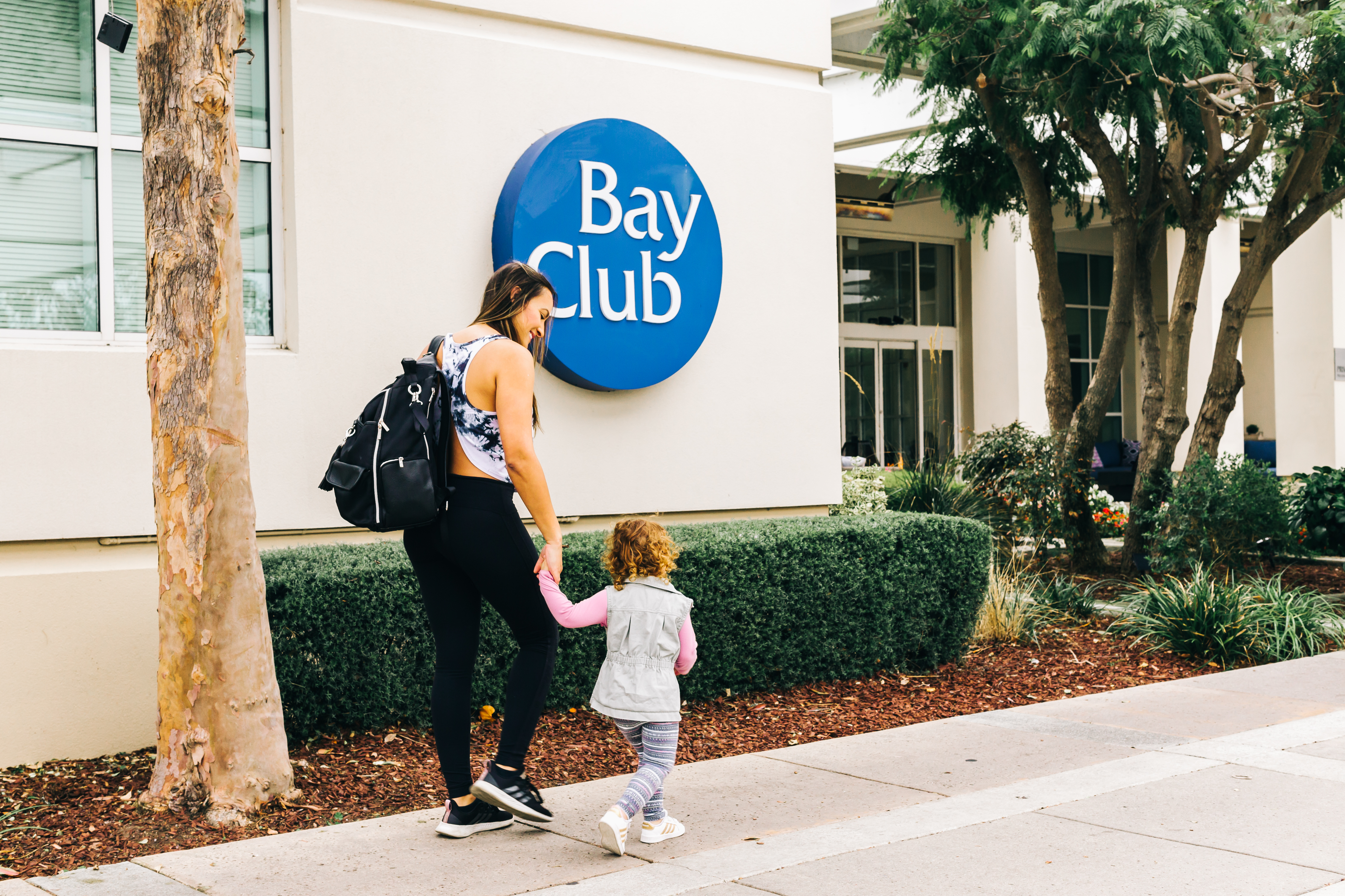 A mother and daughter hold hands walking into the Bay Club Redwood Shores location.