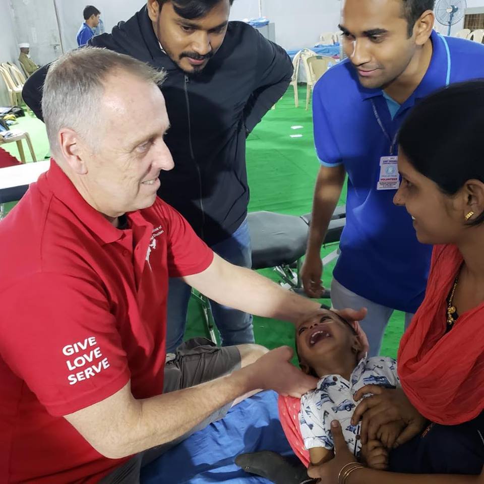 Dr. Scott Donaldson, Vice President of Clinical Operations at Life Chiropractic College West in the San Francisco Bay Area, works with a child during a service trip to India as his family watches and listens. Dr. Donaldson is overseeing Life West's newly launched chiropractic clinic in Delhi.