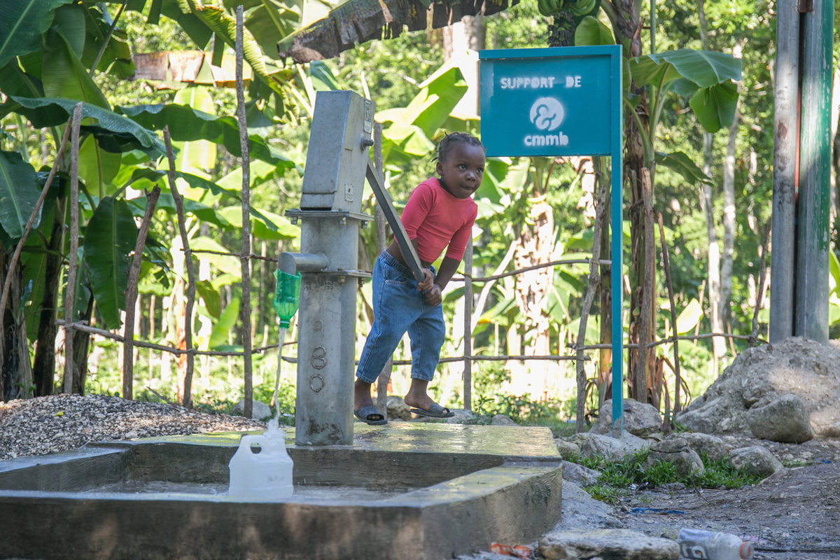 A child collects clean water from a pump constructed by CMMB in Haiti.