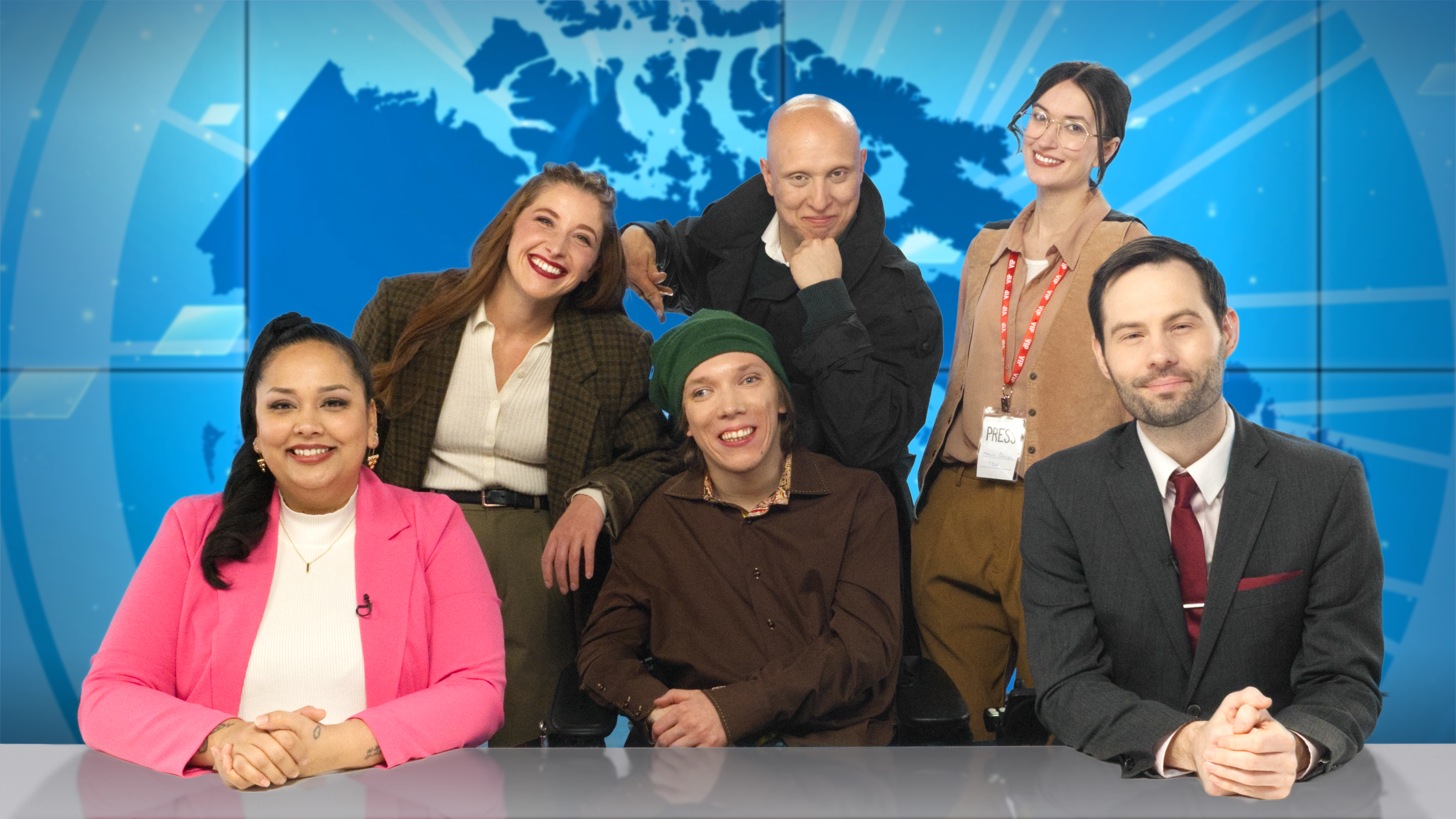 A group of people smile into the camera from behind a news desk.