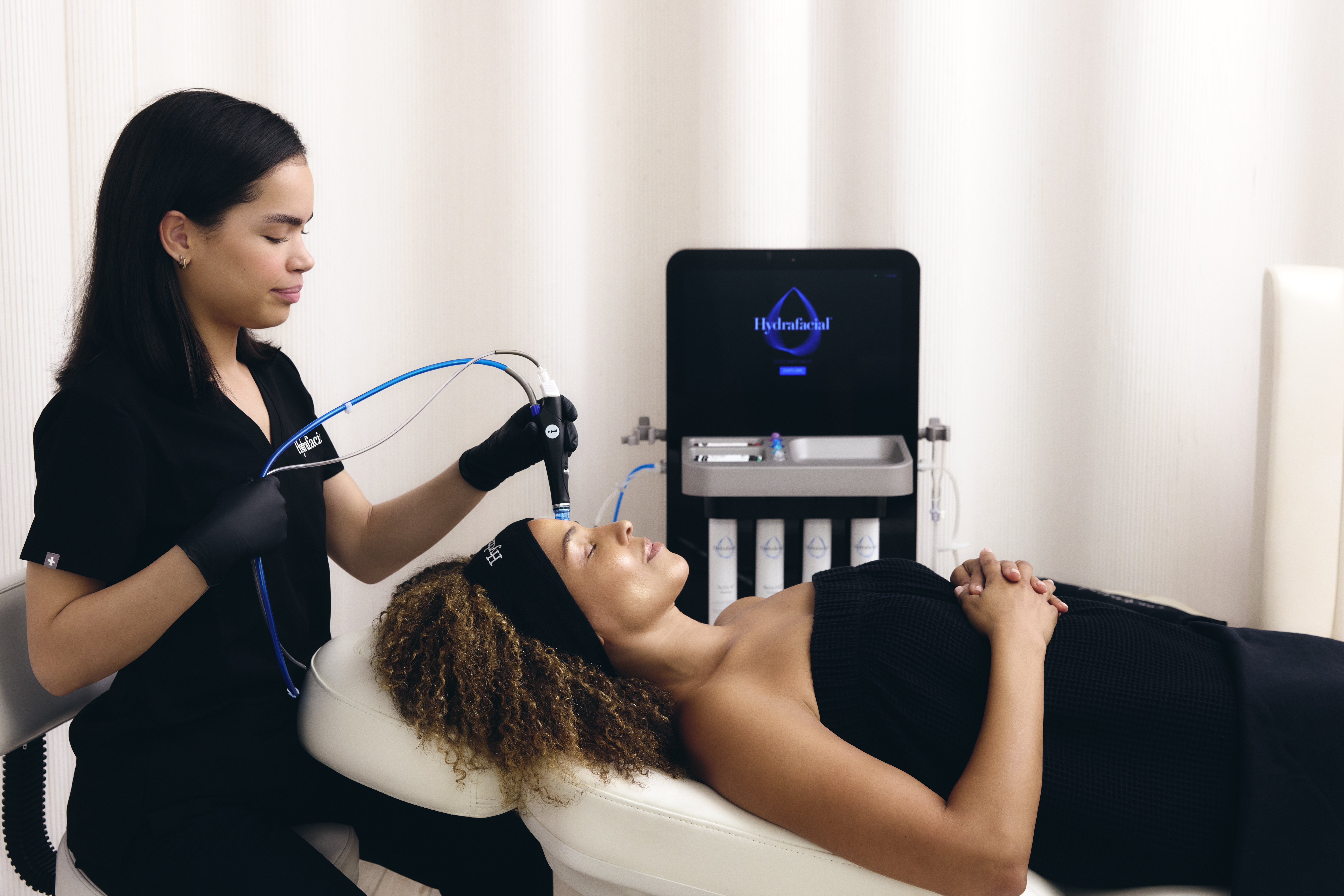 An esthetician uses a Hydrafacial Syndeo device to perform a Hydrafacial skin health treatment on a client.