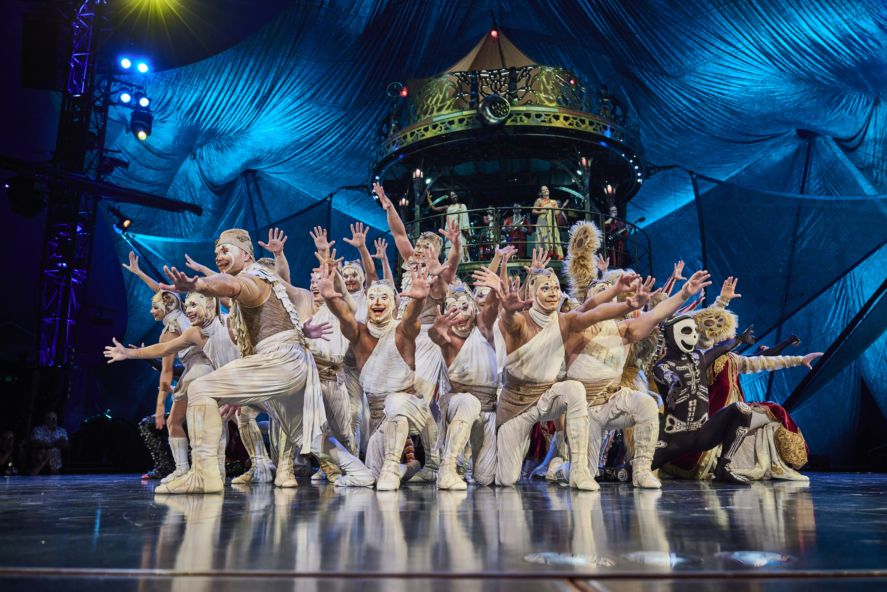 A group of circus performers in elaborate costumes gesture with arms out to the audience in the finale of Cirque du Soleil's KOOZA