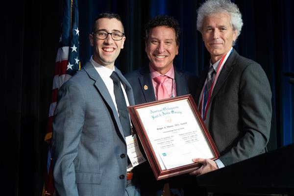 Steven L. Haddad, MD, (center) and J. Chris Coetzee, MD, (right) present the 2019 Roger A. Mann Award given in recognition of the outstanding clinical paper.