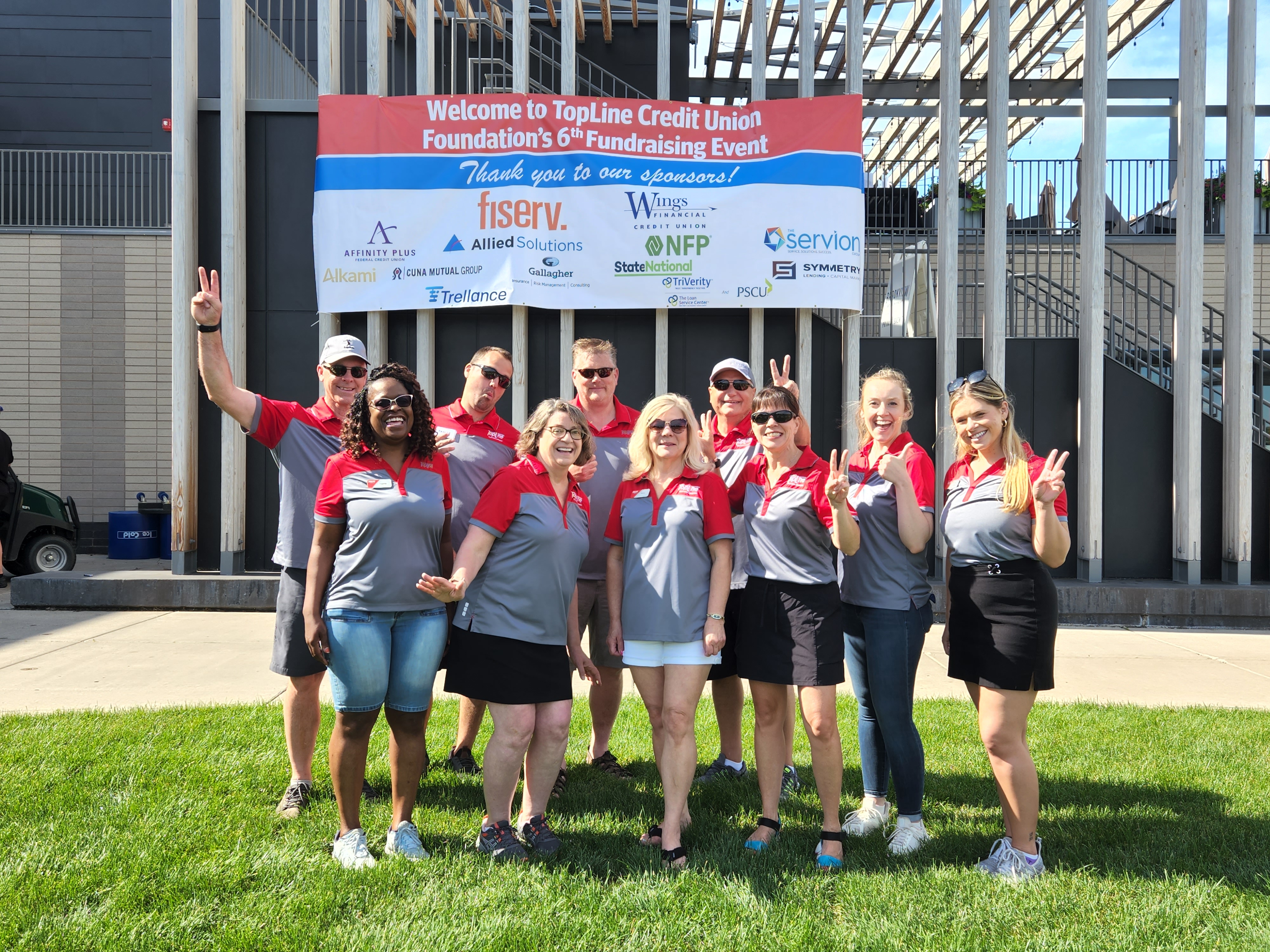 TopLine Credit Union Foundation Board Members stand in front of sponsor banner at event.