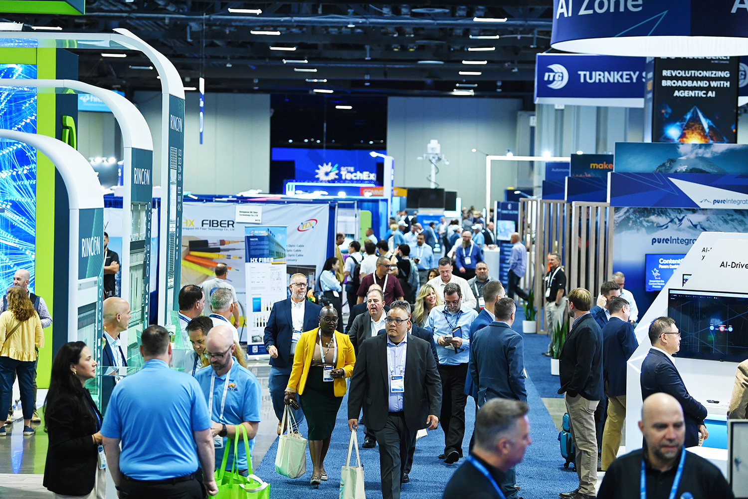 Attendees walking and networking on the exhibition floor of SCTE TechExpo25 surrounded by broadband tech booths and digital displays