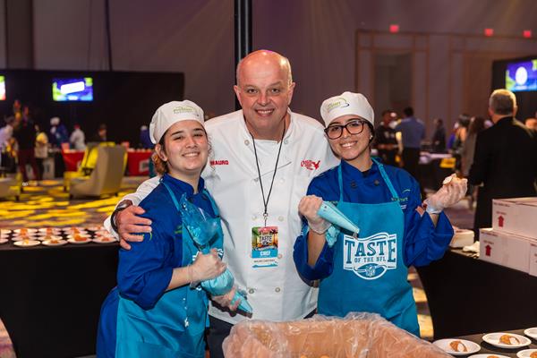 Florida ProStart students pose with Mauro Castano, head decorator and pastry chef from Cake Boss. ProStart students at the table were assigned to fill canolis for guests at the Taste of the NFL. One of the students volunteering was offered a job on the spot. “The food was great at every station,” said Castano. “(The students) were a great help… they made things a lot, lot easier.” 

