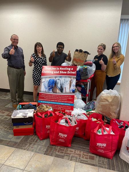 TopLine employees and non-profit partners stand with clothing and shoe drive donations