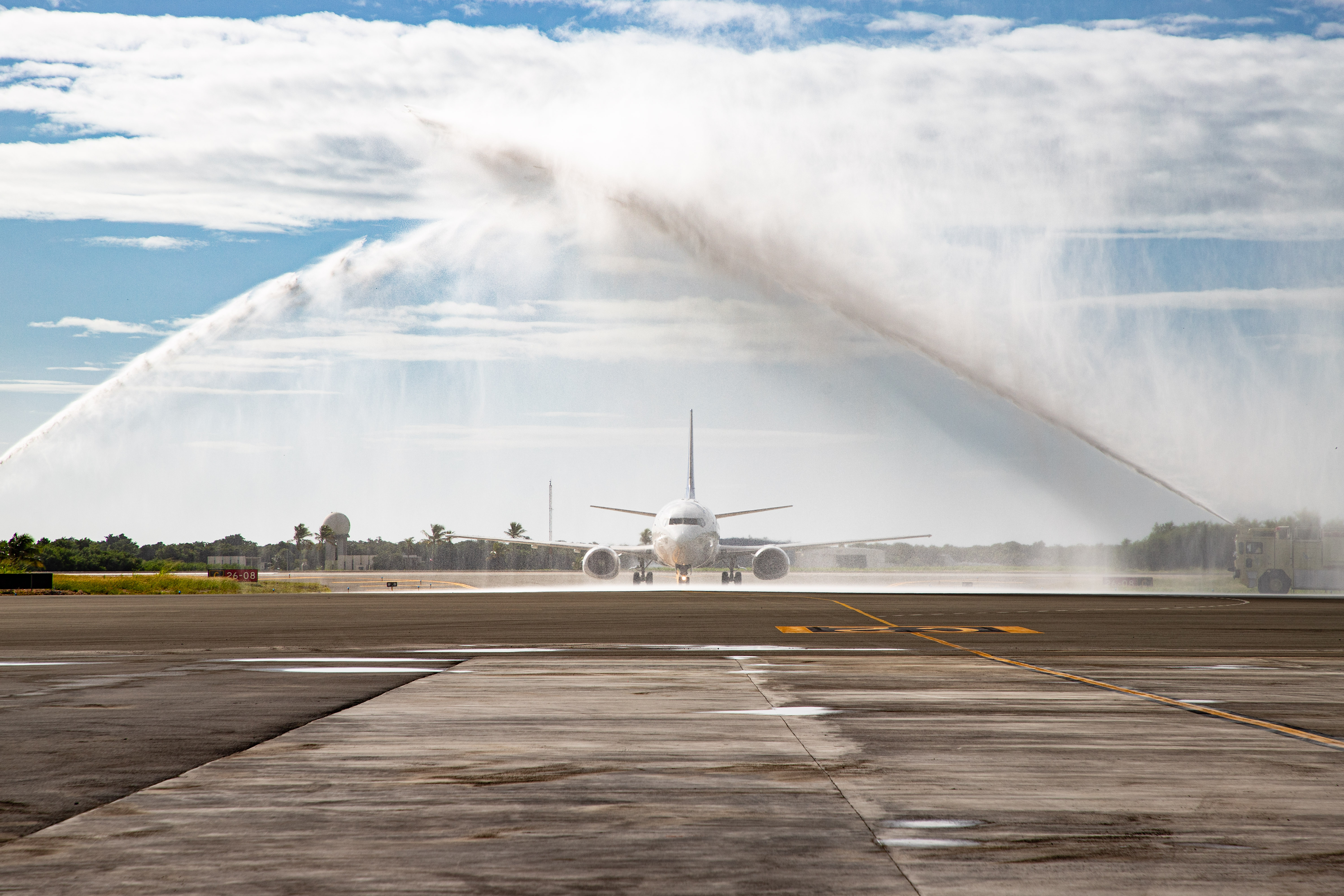 A cargo aircraft taxis on the runway at Punta Cana International Airport as airport fire trucks spray water overhead in a ceremonial welcome.