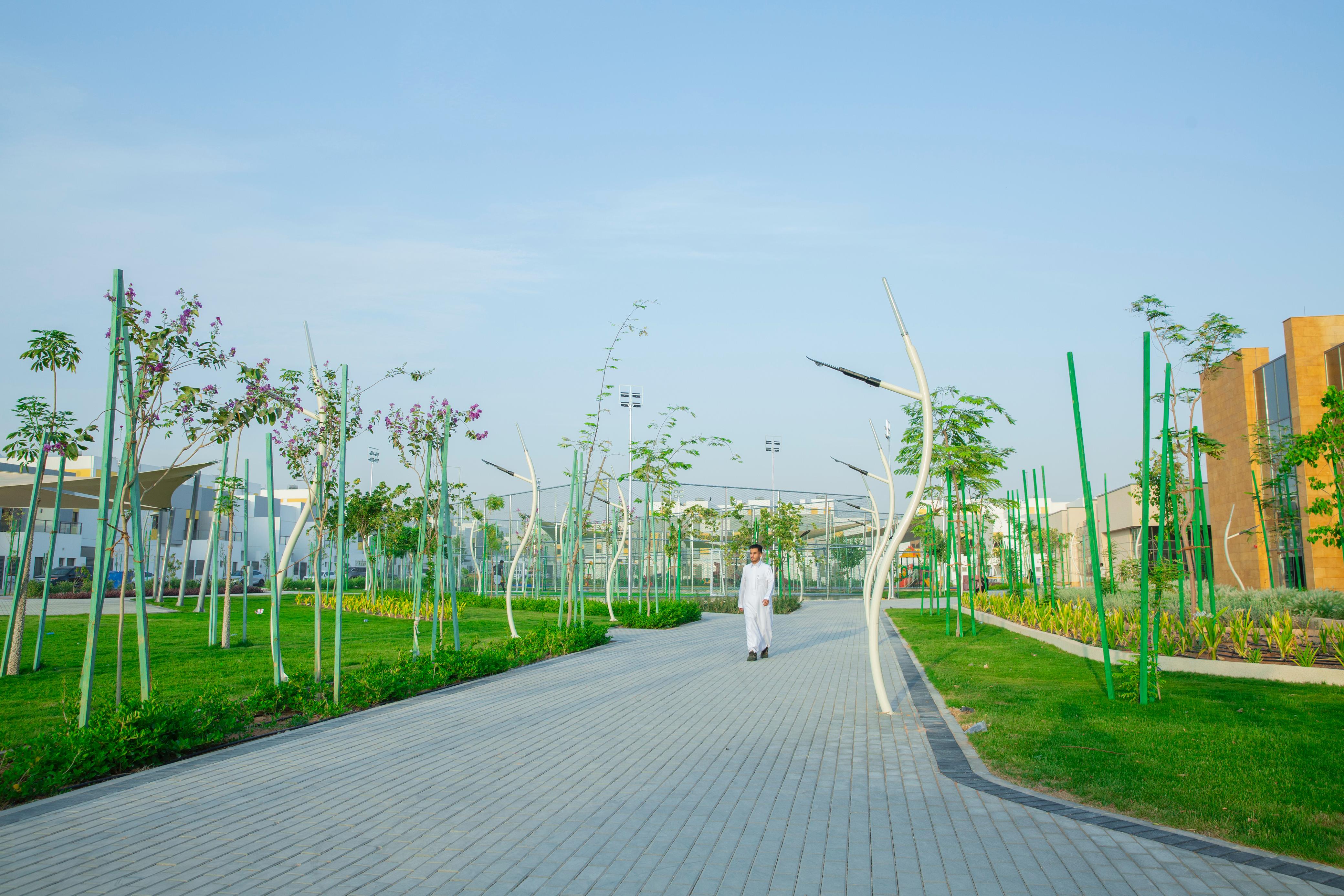A man walks on a paved pathway surrounded by landscaped green areas and unique light poles in an NHC residential community.