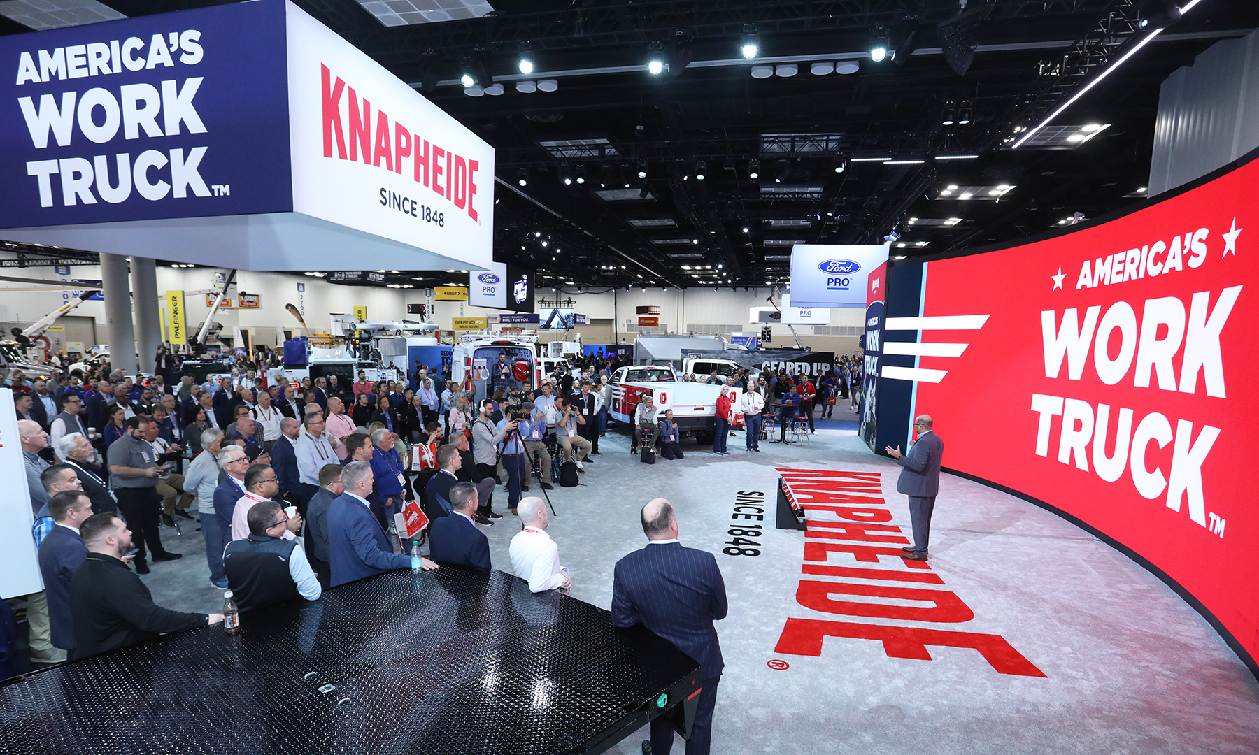 A Knapheide executive standing in front of a large red screen that reads “America’s Work Truck” addresses a Work Truck Week crowd