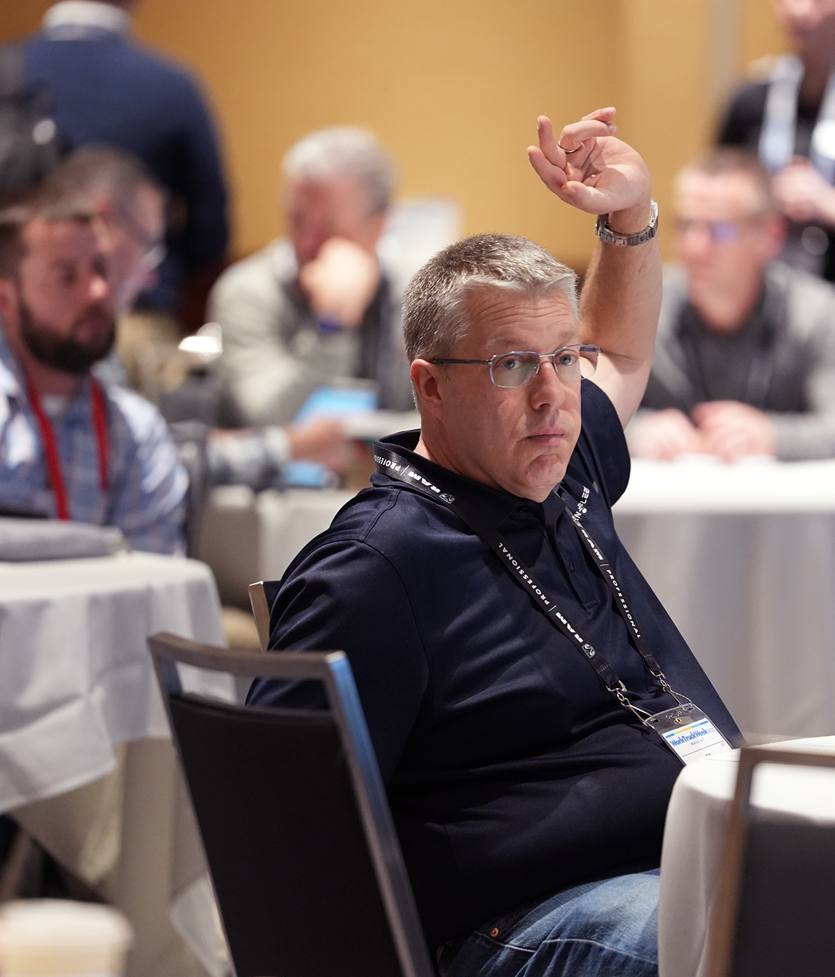 A man wearing a blue golf shirt and Work Truck Week badge raises his hand.