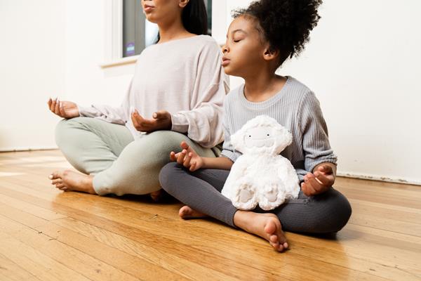 the image shows a mother and a daughter sitting on the floor doing a meditation and practicing mindfulness.