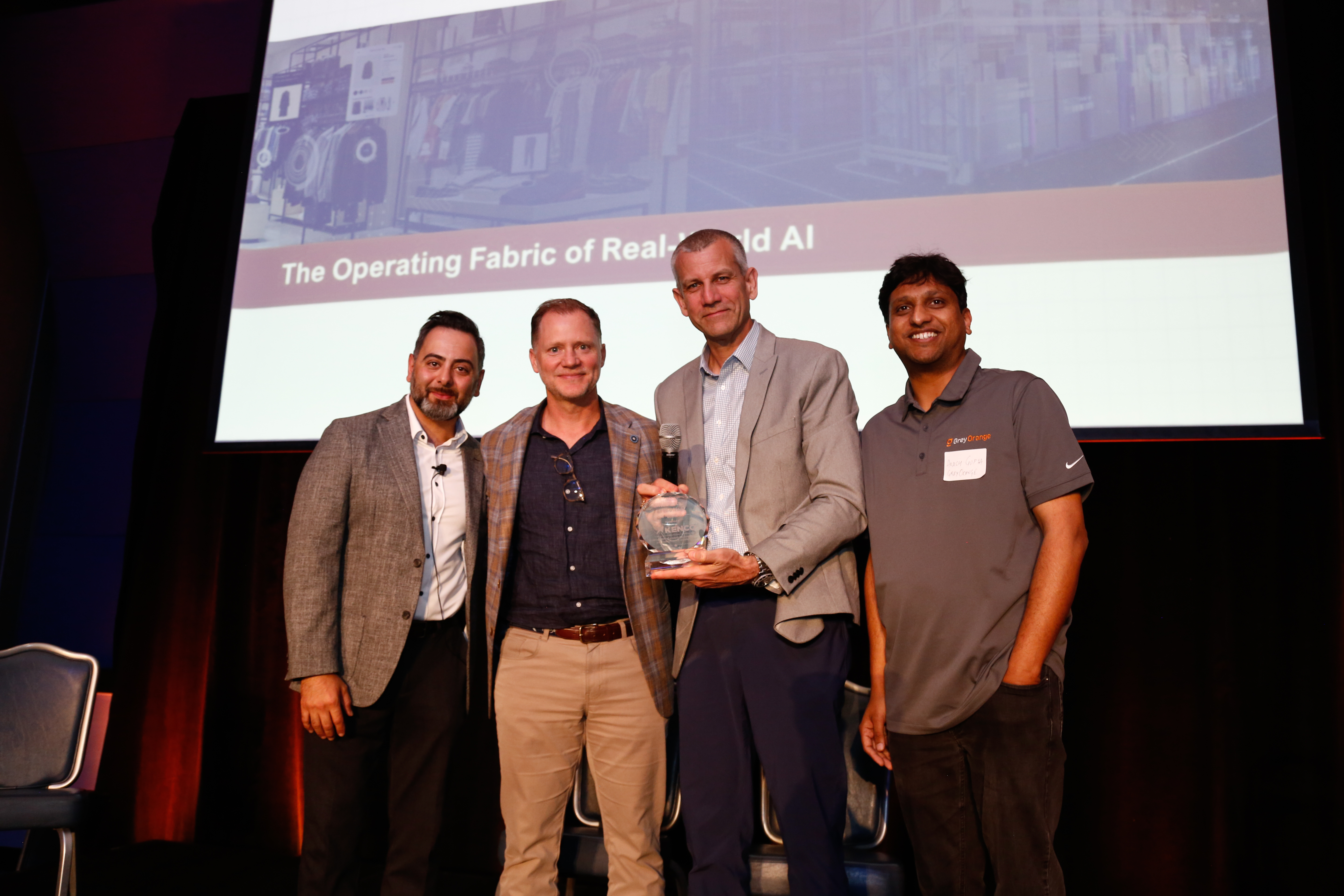 4 men standing in a row, one is holding an award