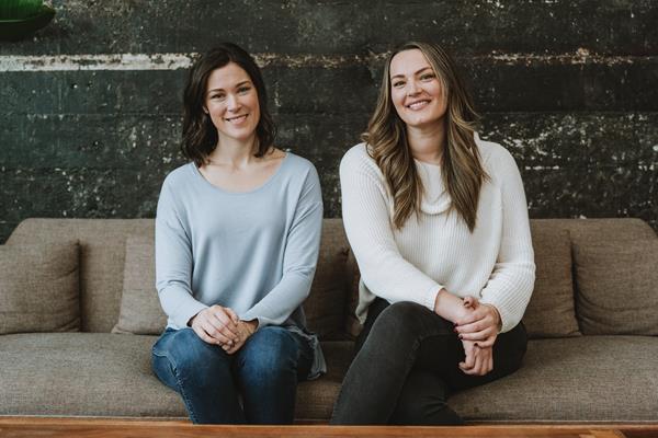 Kelly Oriard and Callie Christensen, two women sit on a couch posing for a photo