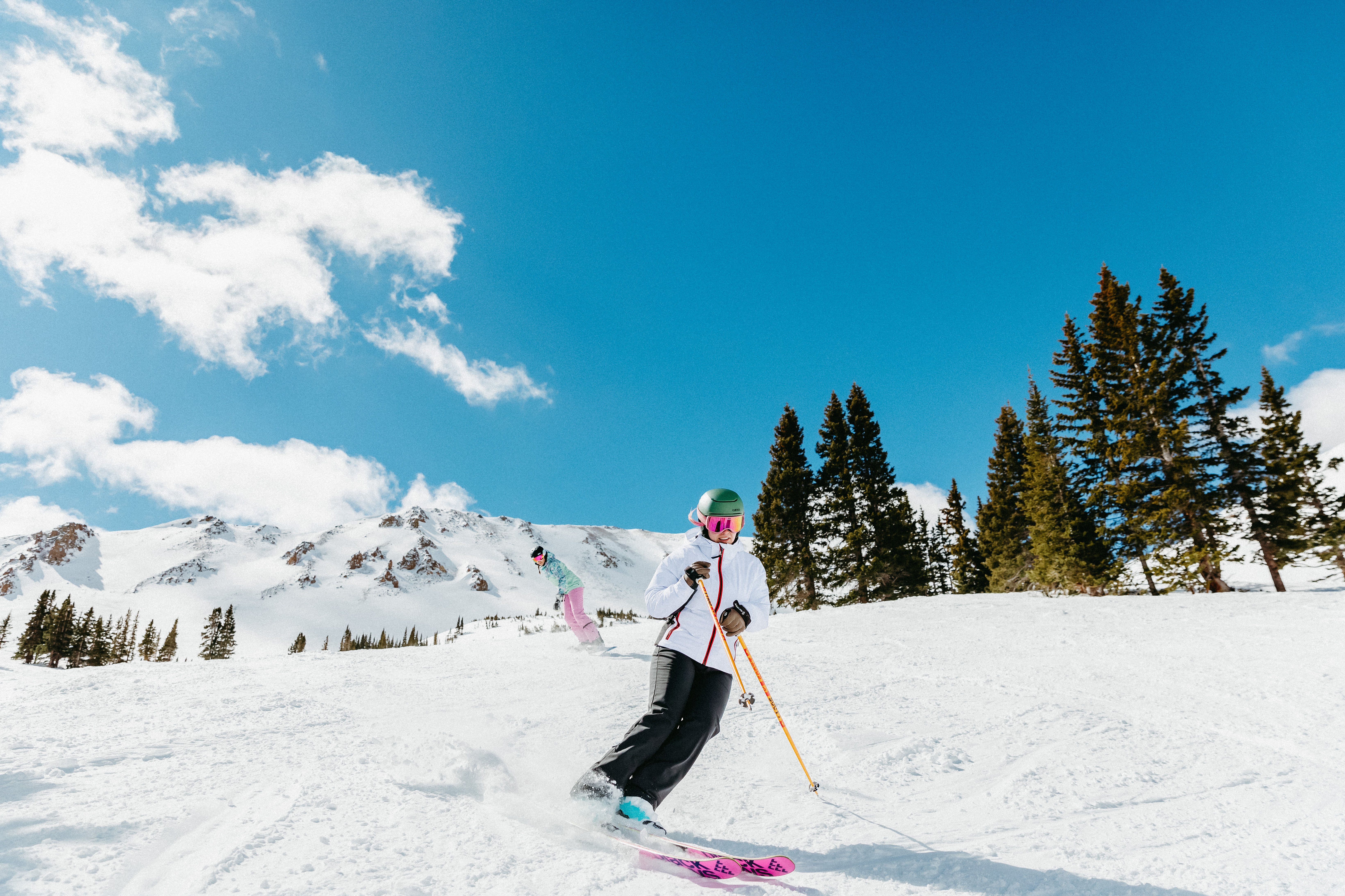 Two women on a ski slope skiing down the mountain in gear and apparel from Christy Sports.