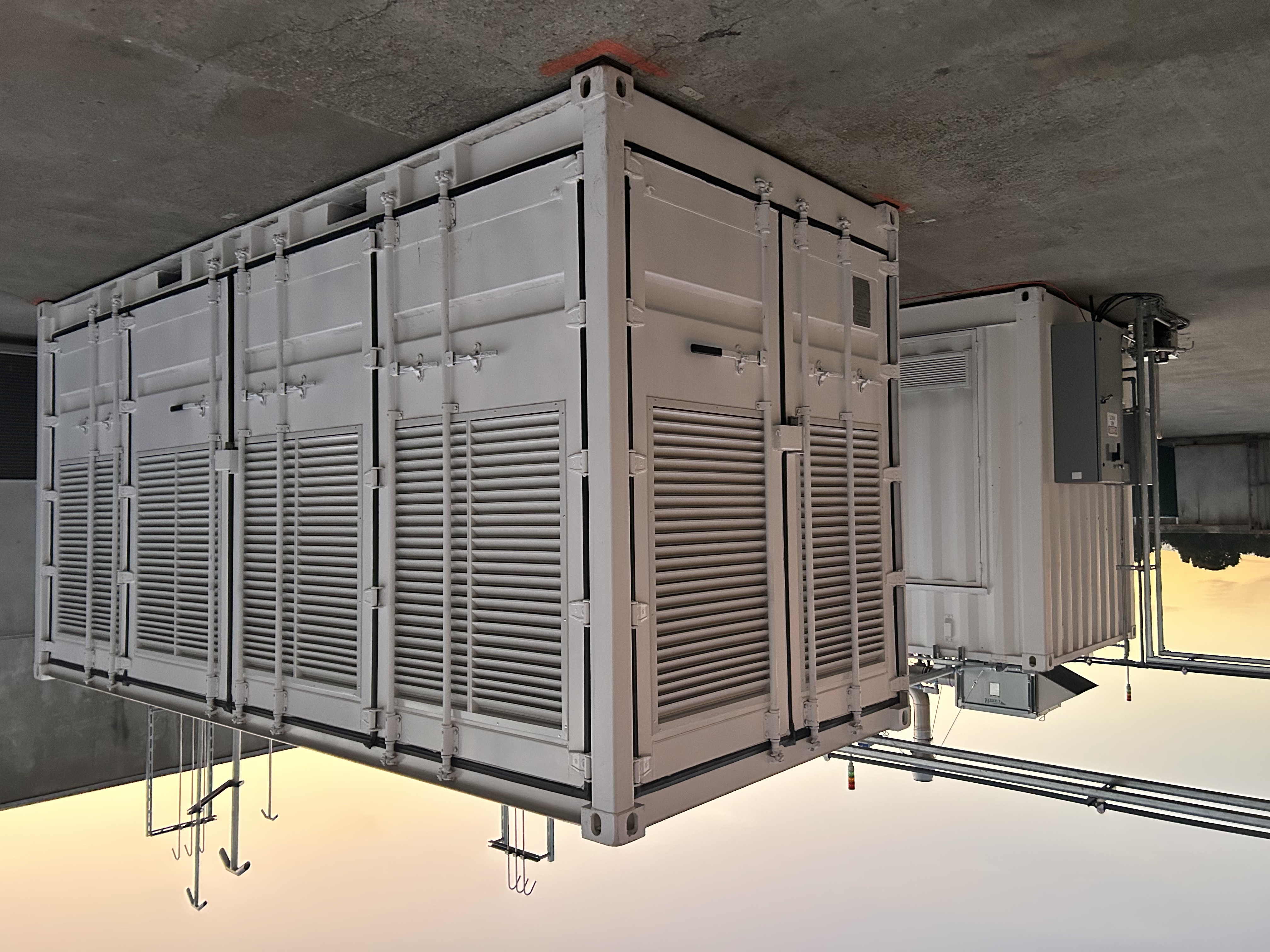 A white, rectangular energy storage container with doors and vents is on concrete outside