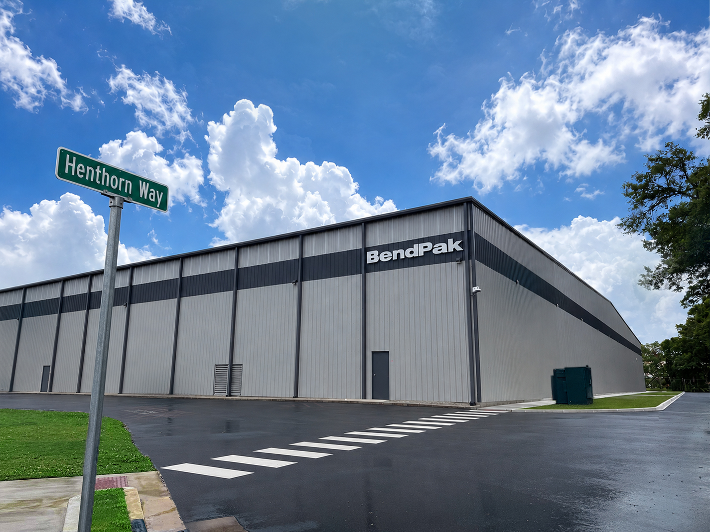A wide-angle view of a newly paved asphalt access road with a green street sign reading Henthorn Way at the BendPak industrial complex.