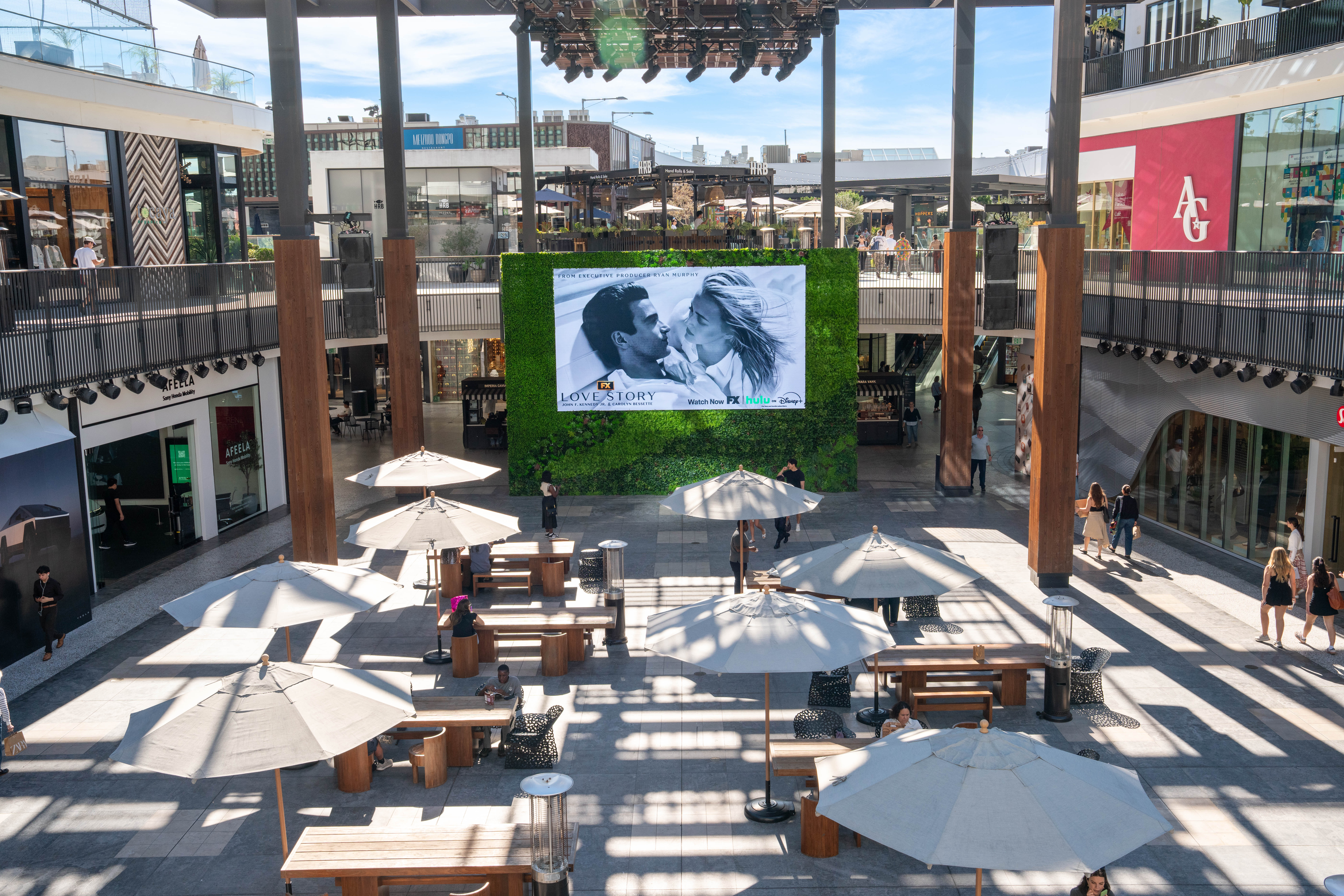 Large digital screen displays FX “Love Story” creative on a green wall backdrop in an open-air retail plaza.