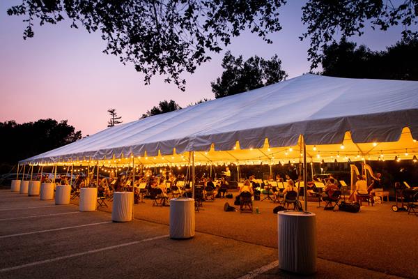 About half of the Westmont Orchestra can safely practice at a time under the big tent. Musicians are six feet apart and masked. Their brass and woodwind instruments are fitted with bell covers. 