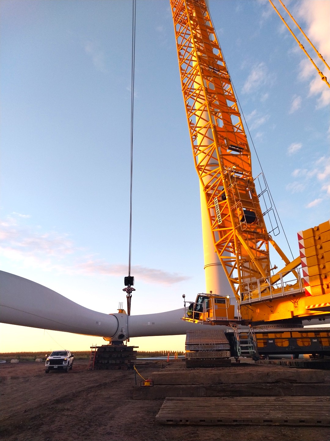 Large crane lifts wind turbine off of truck against a blue sky