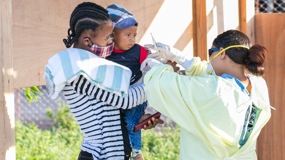 A CMMB health worker with a mother and child at a COVID-19 screening center in Haiti.