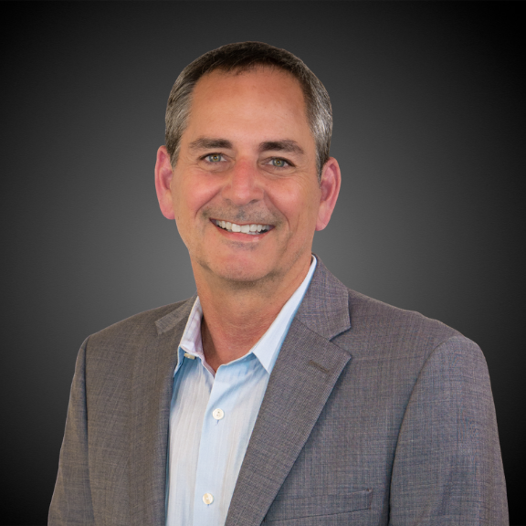Headshot of Mark Wallin, newly named president and general manager of Phillips Connect, smiling in a gray blazer and light blue shirt 