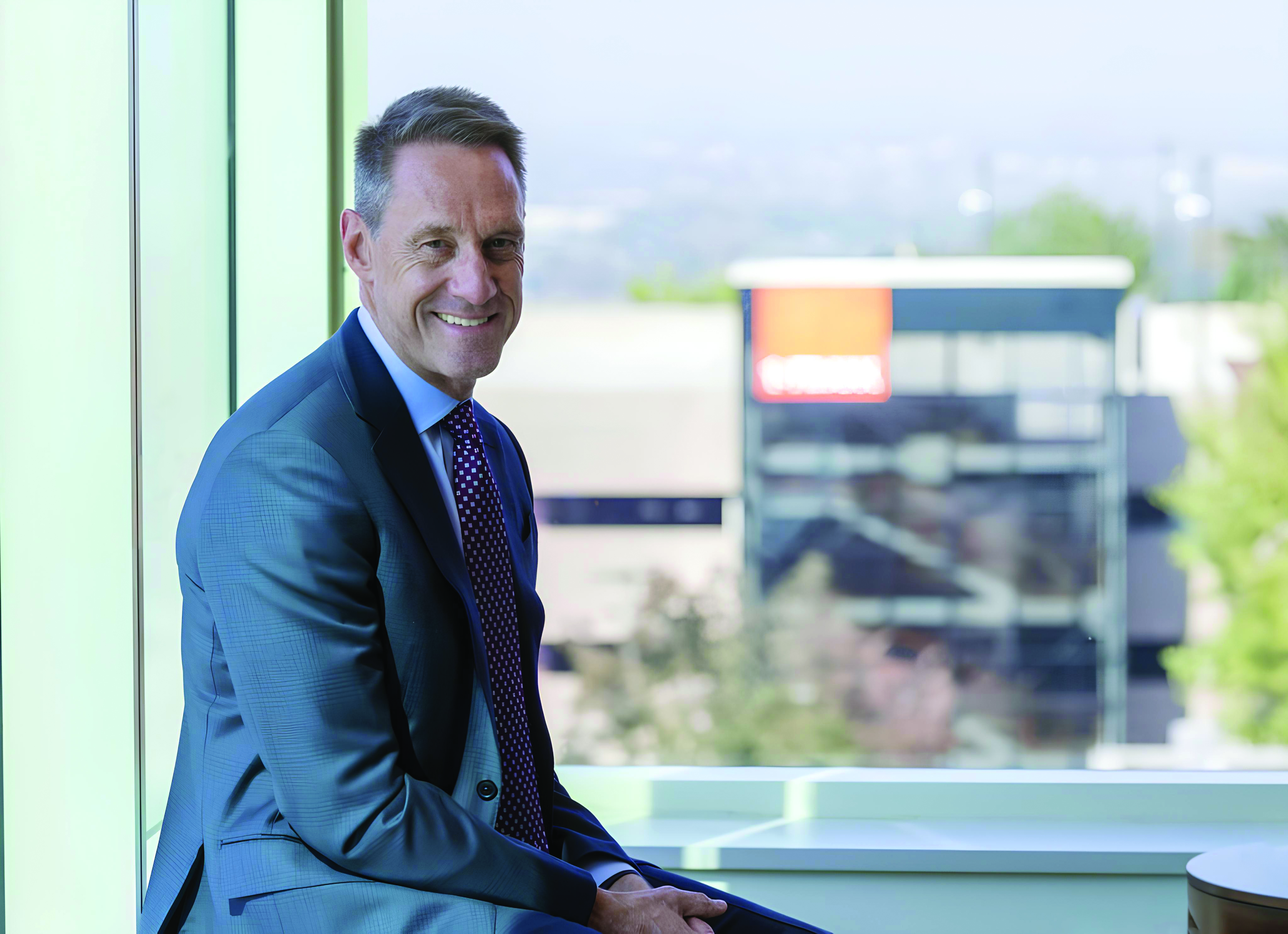 Jim Reuter, former CEO, sits near window with visible FirstBank logo in the distance.  