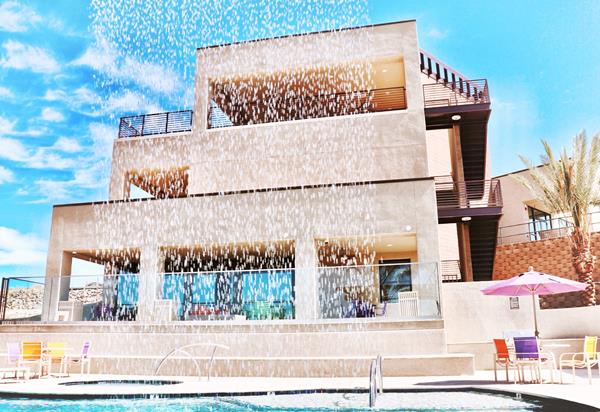 Looking through the poolside waterfall at the modern, 3-story clubhouse with rooftop patio.  