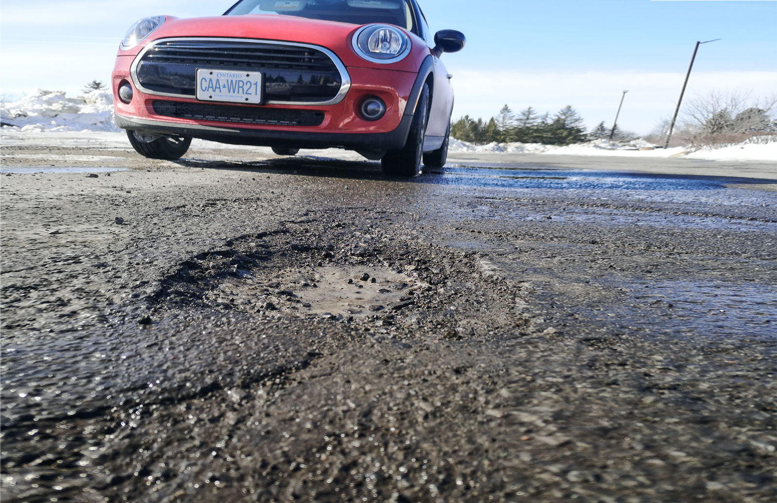 Red car parked by a pothole, with the license plate CAA WR21.