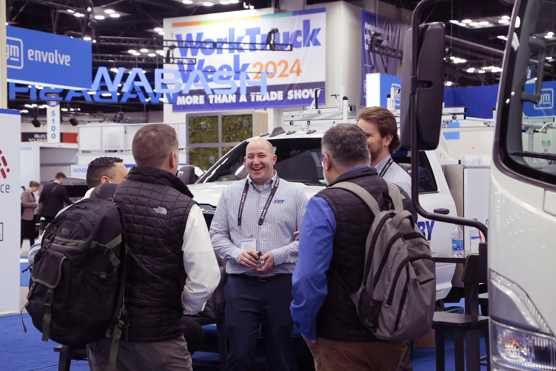 A circle of smiling men talk in front of a truck under a sign that says Work Truck Week