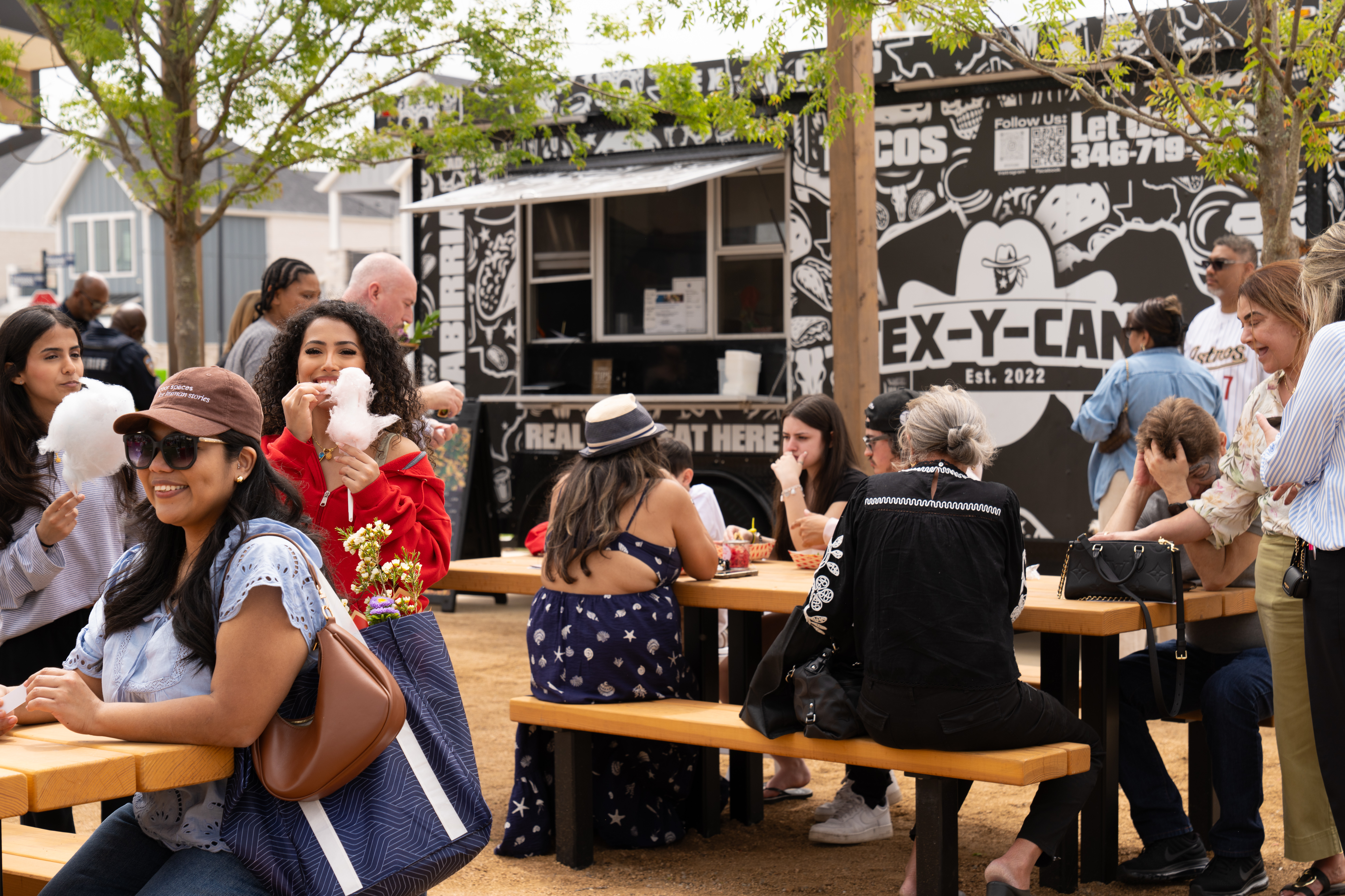People seated at picnic tables near a food truck enjoying food, beverages and conversation.