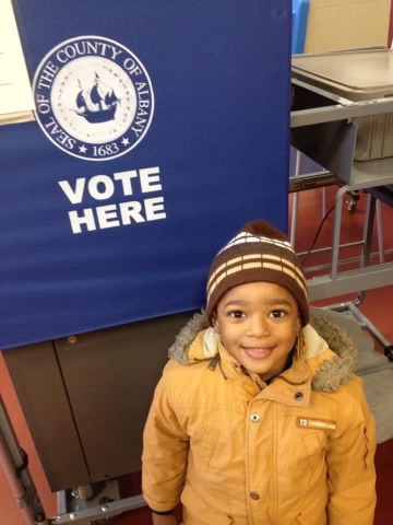 Kenneth and Tracy Braswell's son KJ poses in front of a VOTE HERE sign for the first time.