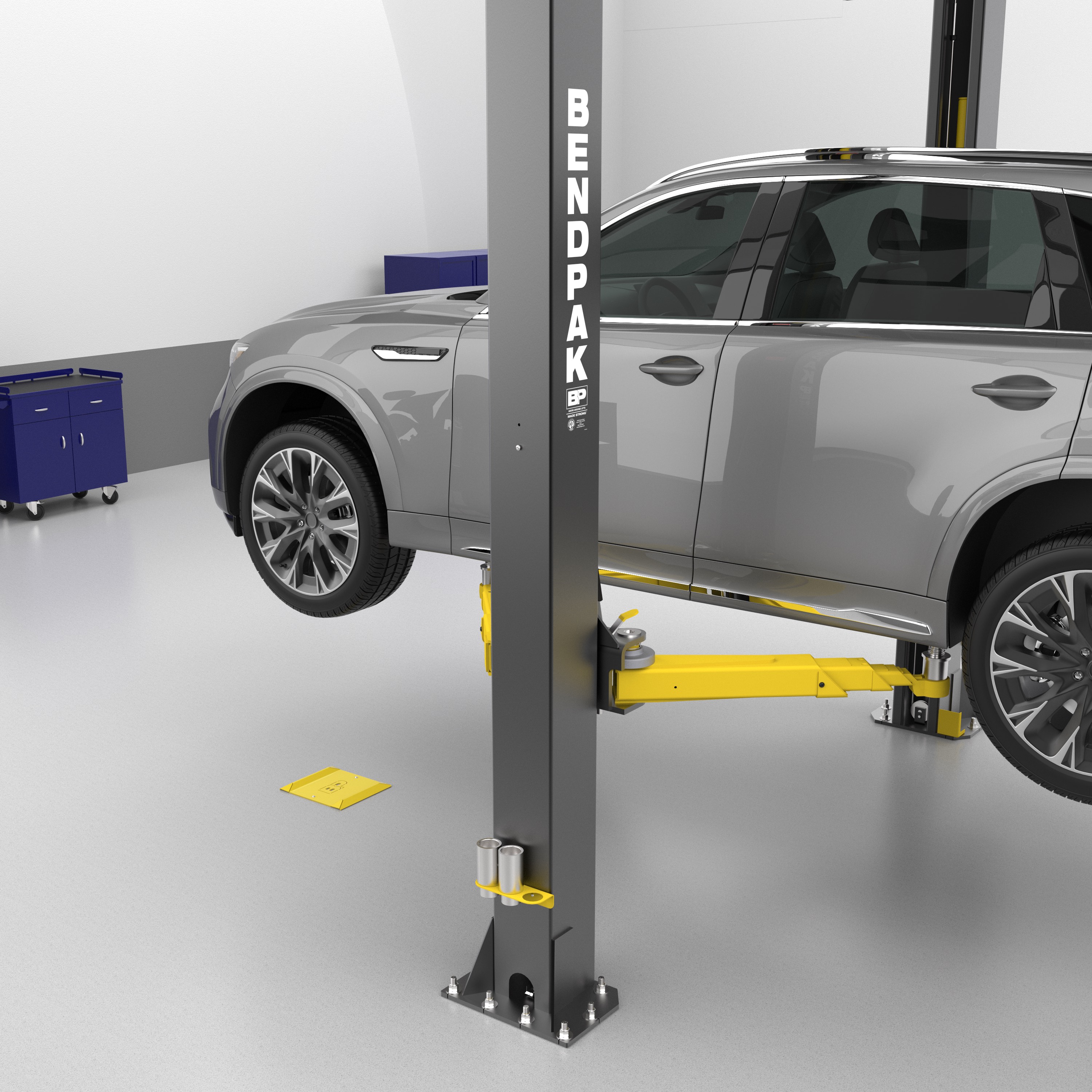 A yellow BendPak spotting dish on a shop floor under a BendPak two-post lift raising an SUV