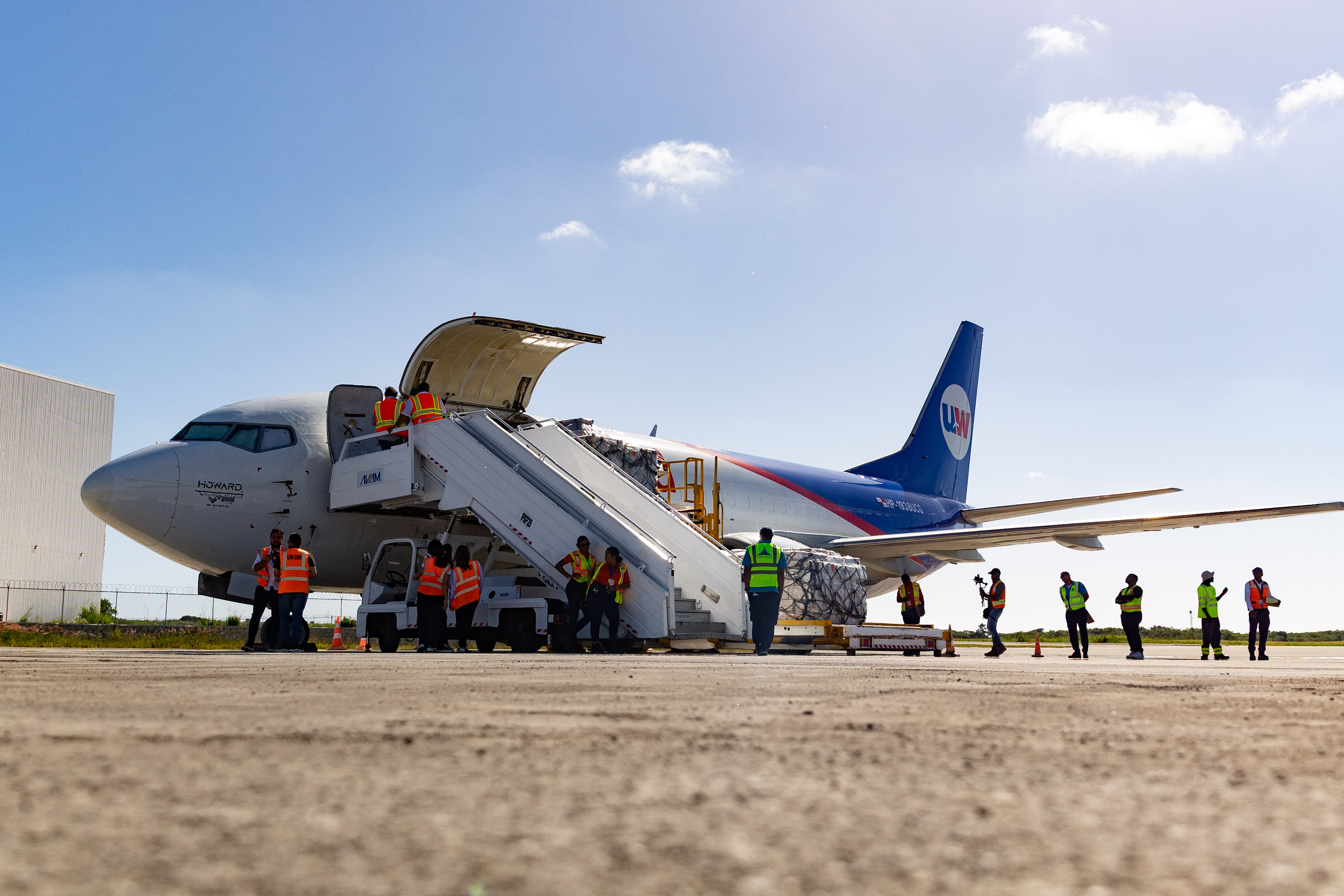 Ground crews unload palletized cargo from a freighter aircraft on the tarmac at the Punta Cana Air Cargo Hub.