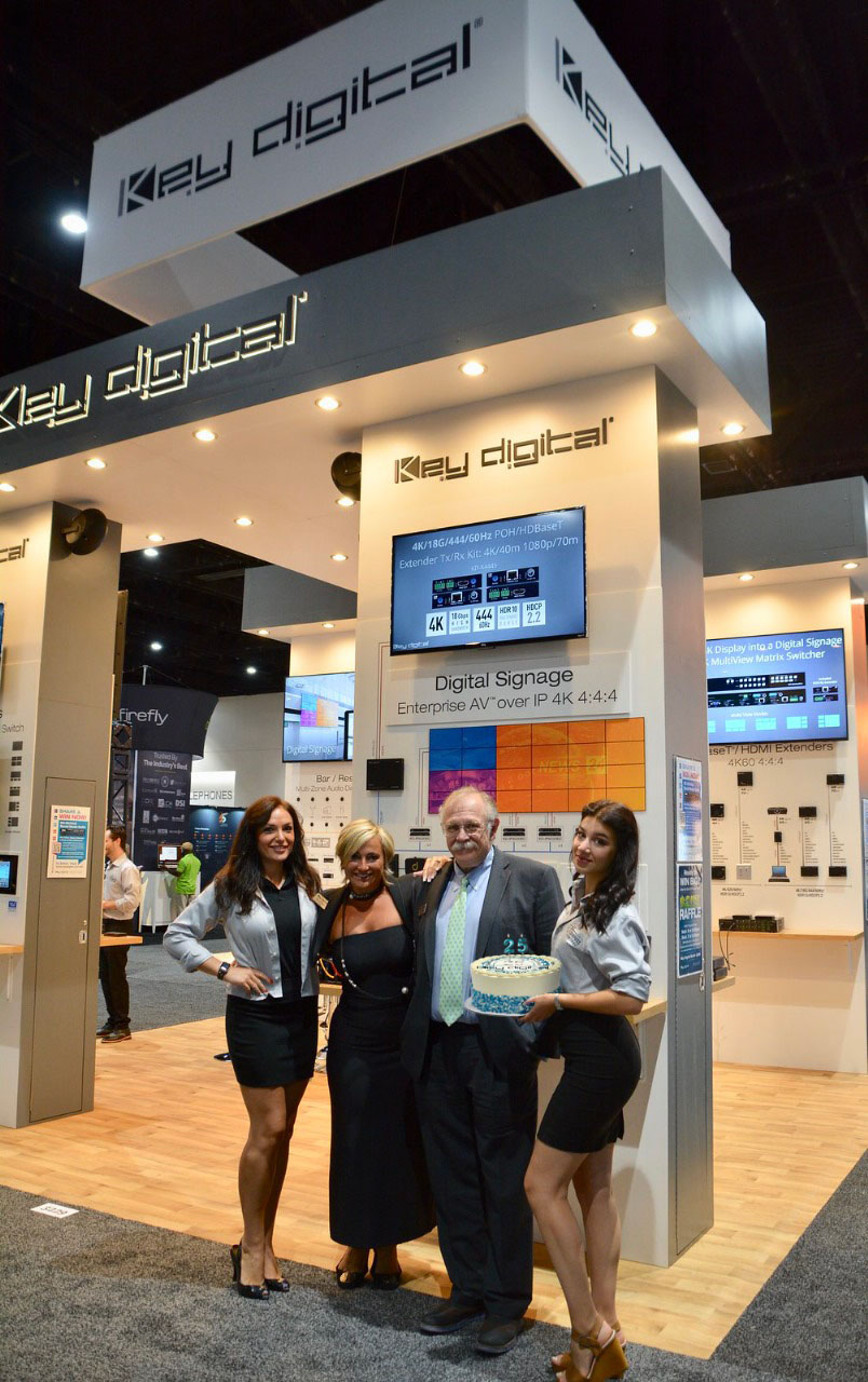 Photo Caption 1: Key Digital COO Masha Tsinberg (middle left) and Mike Tsinberg, founder and president of Key Digital (middle right) flanked by booth staff for the presentation of a cake commemorating Key Digital’s 25th Anniversary