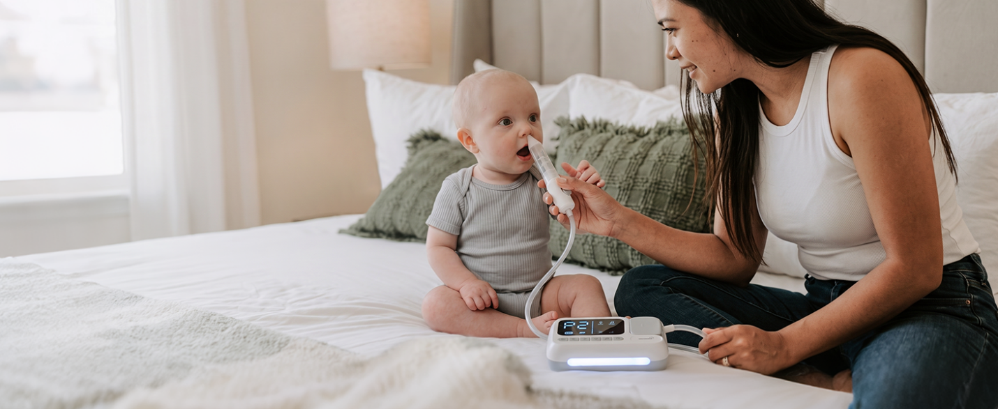 Mother gently using the GROWNSY SniffEase Electric Nasal Aspirator on her baby on the bed