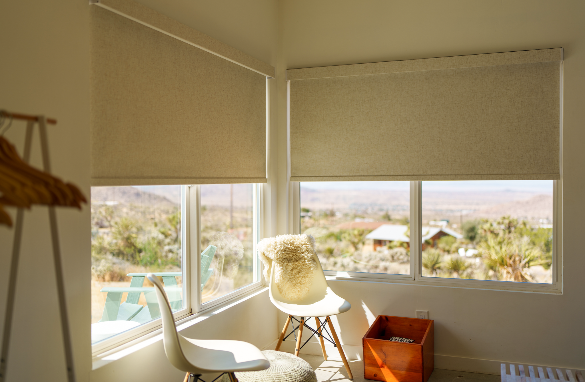 Bright room corner with beige blackout shades on windows, featuring a cozy chair looking out at a desert view