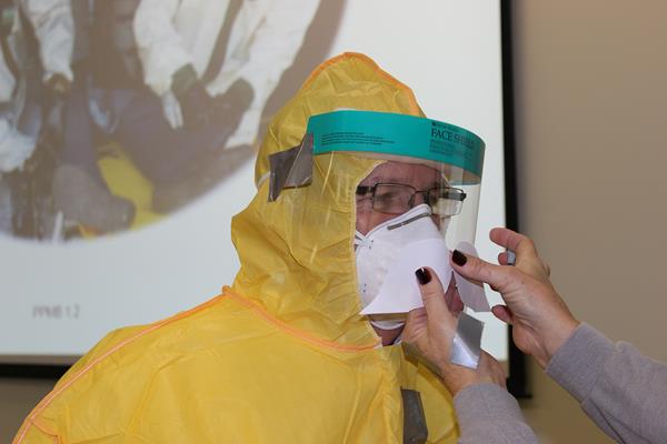 An instructor demonstrates the proper use of a face mask and shield for protecting healthcare workers from infectious diseases or toxins.