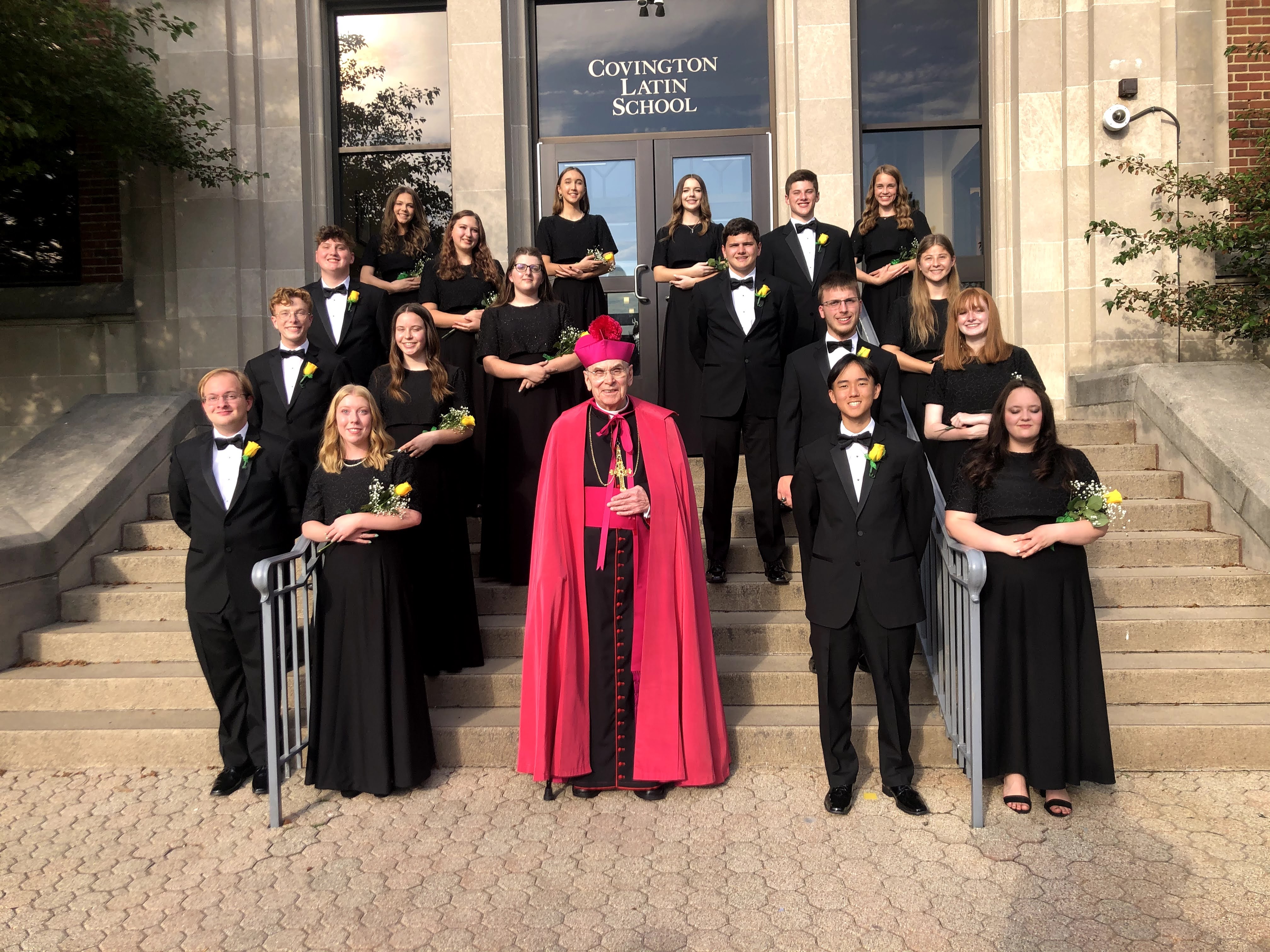 Picture One:
Covington Latin School’s Graduating Class of 2021 – 18 graduating seniors along with Bishop Foys on the steps of Coving Latin School.  Together these seniors received $3.2 million in scholarship offers.
