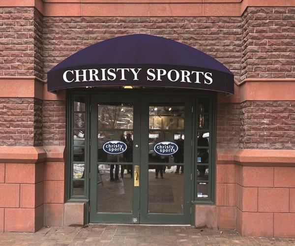 Store entrance of new Christy Sports store in Aspen, Colorado at St. Regis Resort blue awning above store entrance that reads Christy Sports