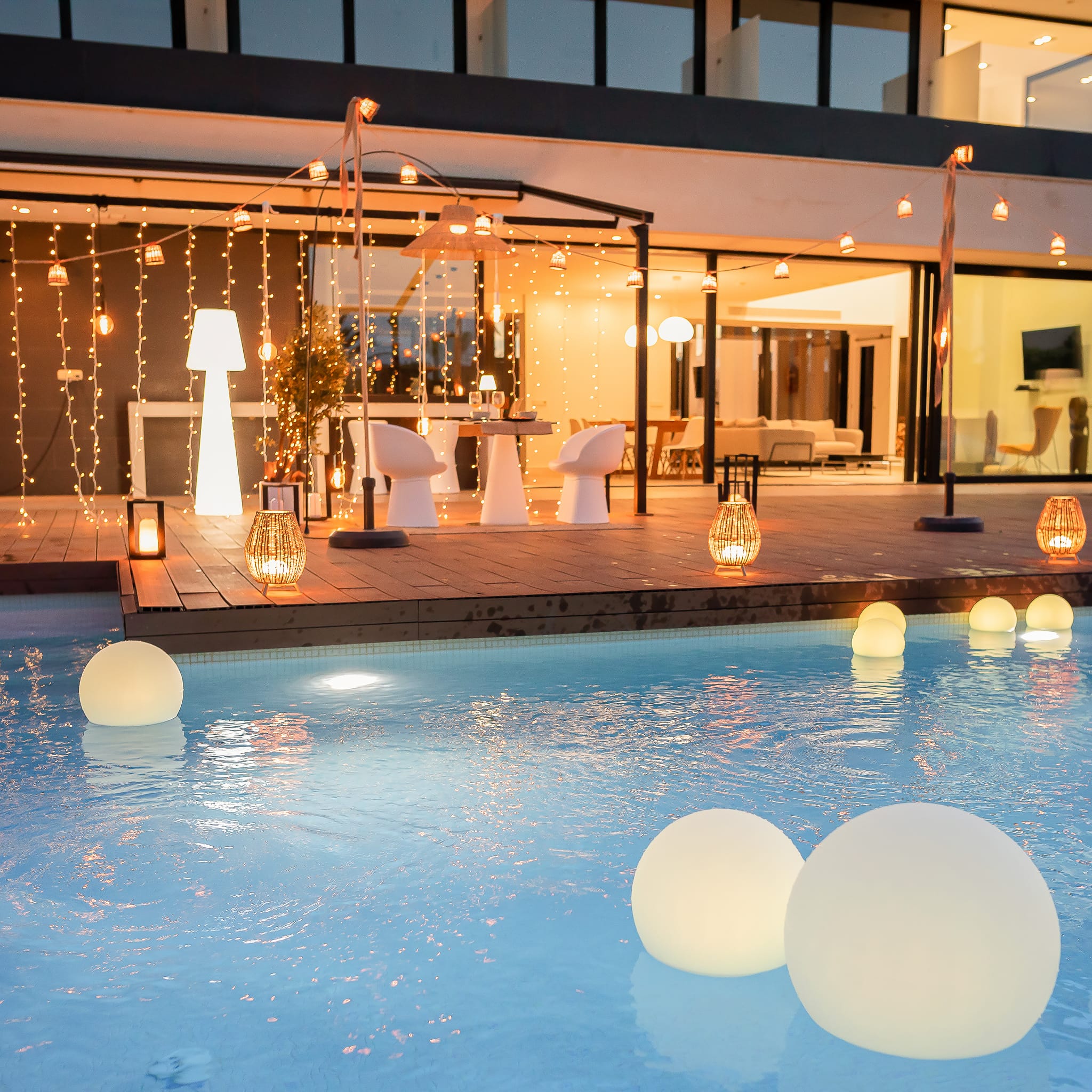 Lampes flottantes solaires Buly et guirlandes LED Newgarden illuminant une terrasse moderne au bord de la piscine.
